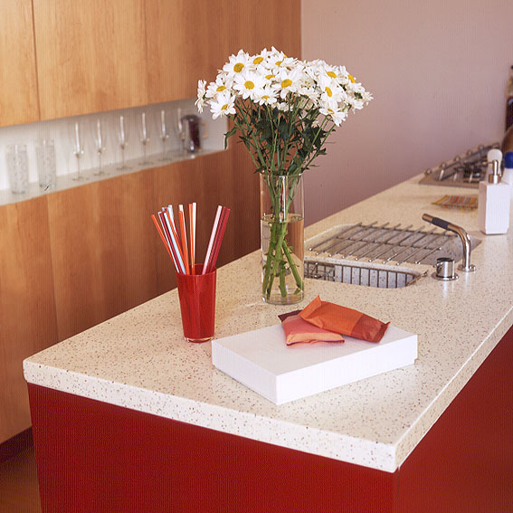 Flowers on red kitchen unit with white marble top.